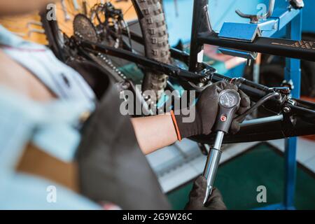 una mano di un meccanico nei guanti utilizzando una pompa con manometro per regolare la sospensione posteriore Foto Stock