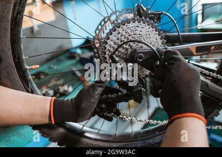 la mano del meccanico di bicicletta maschio nei guanti collega la catena al pignone Foto Stock