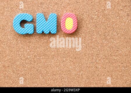 Alfabeto di schiuma giocattolo a colori con la parola OGM (abbreviazione di organismi geneticamente modificati) sullo sfondo del pannello di sughero Foto Stock