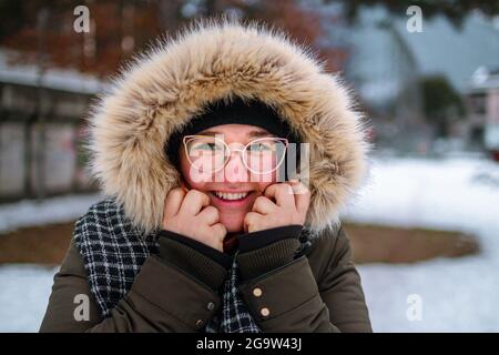 Felice giovane donna sorridendo e proteggendo la sua mano dal freddo sotto una giacca di furry in inverno come ha dimenticato di indossare i guanti Foto Stock