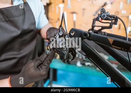 la mano di un meccanico nei guanti tira un cavo mentre si regola il deragliatore posteriore Foto Stock