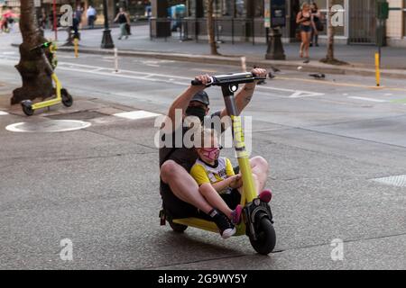 Seattle, Stati Uniti. 27 luglio 2021: Una persona in sella a uno scooter condiviso sul marciapiede con un bambino per obiettivo. I nuovi scooter share non dovrebbero essere guidati sui marciapiedi, ma le aziende non sono inoltre tenute a fornire caschi per i piloti per conformarsi alle leggi locali sui caschi. In questo modo i piloti si trovano in un luogo difficile per cavalcare i marciapiedi in pericolo di pedoni o per guidare nel traffico con veicoli in pericolo e quindi infrangendo le leggi sul casco. Credit: James Anderson/Alamy Live News Foto Stock