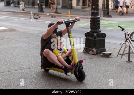 Seattle, Stati Uniti. 27 luglio 2021: Una persona in sella a uno scooter condiviso sul marciapiede con un bambino per obiettivo. I nuovi scooter share non dovrebbero essere guidati sui marciapiedi, ma le aziende non sono inoltre tenute a fornire caschi per i piloti per conformarsi alle leggi locali sui caschi. In questo modo i piloti si trovano in un luogo difficile per cavalcare i marciapiedi in pericolo di pedoni o per guidare nel traffico con veicoli in pericolo e quindi infrangendo le leggi sul casco. Credit: James Anderson/Alamy Live News Foto Stock