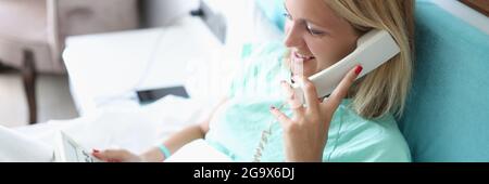 Donna a letto che parla al telefono in camera d'albergo Foto Stock