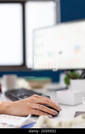 Dirigente aziendale nel suo ufficio utilizzando e facendo clic sul mouse con bluetooth. Dito della mano che spinge il mouse mentre l'imprenditore sta leggendo le statistiche, sullo schermo del computer sul posto di lavoro . Foto Stock