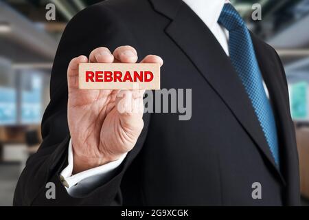 Uomo d'affari mostra un blocco di legno con la parola rebrand. Branding, marketing, business concept. Foto Stock