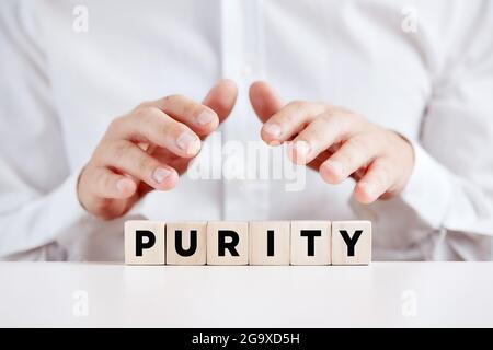 Uomo che tiene le mani sui cubetti di legno con la parola purezza. Foto Stock