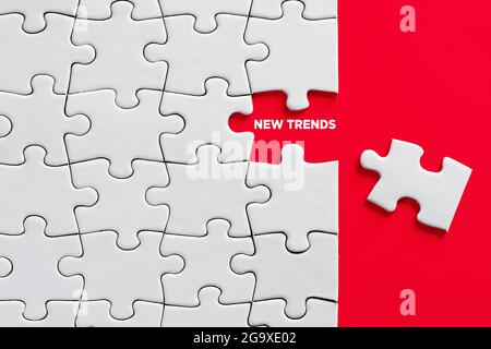 Per scoprire nuovi concetti di tendenza. La parola nuove tendenze scritto su pezzo di puzzle mancante su sfondo rosso. Foto Stock