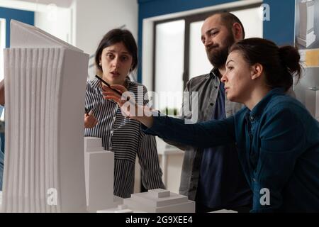 Team professionale di architetti che analizzano il modello di costruzione della maquette. Gruppo di partner ingegneri che lavorano alla progettazione di progetti per il piano di costruzione, spiegando la visione di un progetto moderno. Foto Stock