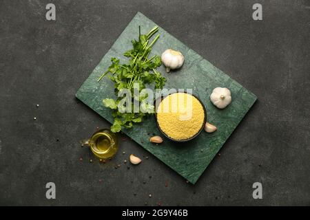 Composizione con couscous crudo, spezie e olio su fondo scuro Foto Stock