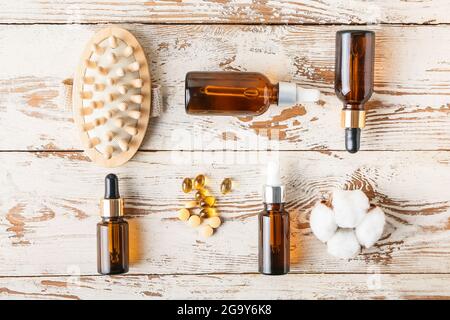 Bottiglie cosmetiche contagocce, pillole e fiore di cotone su sfondo di legno chiaro Foto Stock