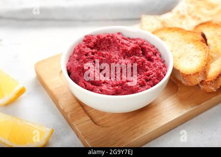 Ciotola con gustoso hummus di barbabietola e tostature su sfondo chiaro, primo piano Foto Stock