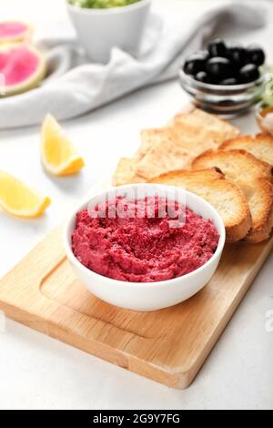 Ciotola con gustoso hummus di barbabietola, cracker e toast su sfondo chiaro Foto Stock