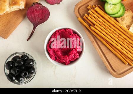 Composizione con saporito hummus di barbabietola, olive e bastoncini di pane su sfondo chiaro Foto Stock