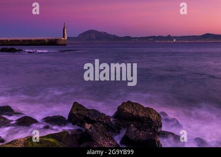 Onde che si infrangono sulla spiaggia di Playa Chica con la statua del Sacro cuore di Gesù e Punta del Santo in lontananza, Tarifa, cadice, Andalusia, Spagna Foto Stock