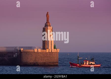 Barca da pesca che naviga nel porto passando la statua del Sacro cuore di Gesù e Punta del Santo in lontananza, Tarifa, cadice, Andalusia, Spagna Foto Stock