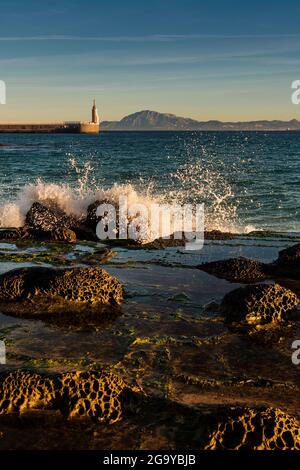 Onde che si infrangono sulla spiaggia di Playa Chica con la statua del Sacro cuore di Gesù e Punta del Santo in lontananza, Tarifa, cadice, Andalusia, Spagna Foto Stock