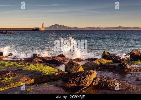 Onde che si infrangono sulla spiaggia di Playa Chica con la statua del Sacro cuore di Gesù e Punta del Santo in lontananza, Tarifa, cadice, Andalusia, Spagna Foto Stock