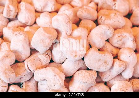 Zucchero a velo ricopre un mucchio di amaretti irregolari alle mandorle in un mercato italiano, con superfici pallide e incrinate mostrate in primo piano. Foto Stock