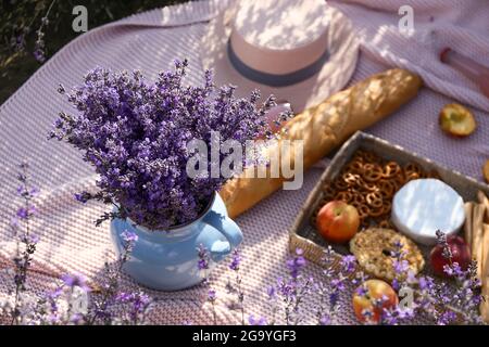 Caraffa con fiori di lavanda e cibo gustoso per un picnic romantico in campo Foto Stock