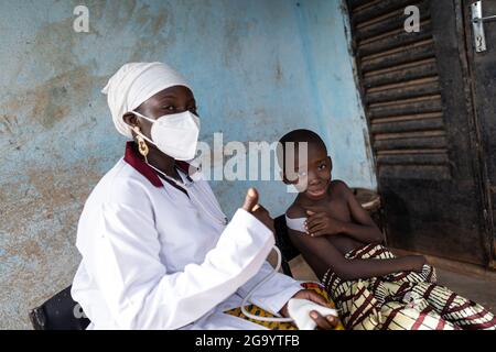 In questa immagine un piccolo ragazzo africano sorridente con un grande intonaco sulla spalla è seduto accanto al suo pediatra indossando una maschera facciale con il pollice su a. Foto Stock