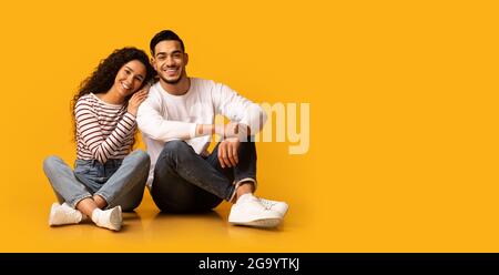 Happy giovani sposi mediorientali seduti al piano su sfondo giallo Foto Stock