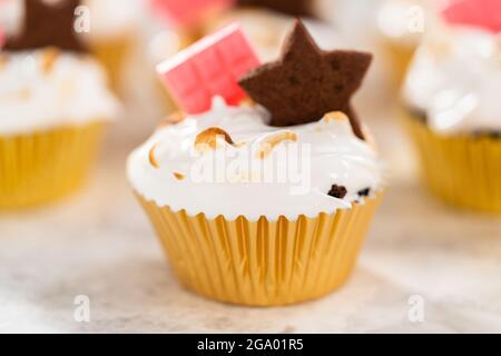 Cupcake gourmet s'Mores con glassa di meringa e guarnita con cracker di cioccolato graham a forma di stella e una mini barretta di cioccolato rosa. Foto Stock