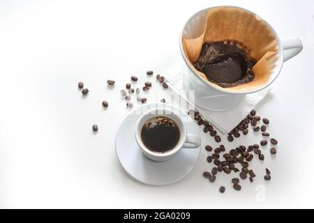 Caffè in una tazza e caffè macinato in un sacchetto con filtro, bevanda calda con getto a goccia, sfondo chiaro sbiadito a bianco con alcuni chicchi, spazio per la copia, messa a fuoco selezionata Foto Stock