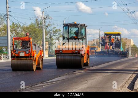 Processo di asfaltatura, asfaltatrice e due rulli stradali durante i lavori di costruzione di strade, lavorando sul nuovo cantiere stradale, piazzando un Foto Stock