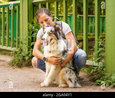 Felice donna seduta abbracciando con il giovane bel cane Pastore Australiano in prato Foto Stock