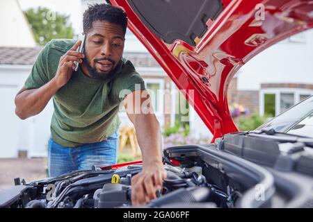 Uomo che guarda il motore dopo l'auto guasto chiamata recupero automatico sul telefono cellulare Foto Stock