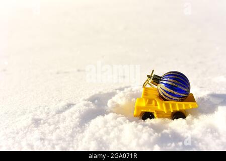 Camion giocattolo con una palla di Natale sullo sfondo di neve bianca nella foresta. Сoncept di prepararsi per la celebrazione del nuovo anno. Regali di shopping, decoratin Foto Stock