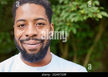 Testa e spalle Ritratto di sorridente giovane uomo in piedi all'aperto in giardino Foto Stock