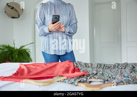 Primo piano di Donna fotografando abiti indesiderati con il telefono cellulare per vendere online Foto Stock
