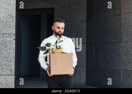 Lavoratore maschio senza lavoro che si sposta fuori ufficio con scatola piena di effetti personali, ha perso lavoro e lasciato senza soldi, spazio di copia Foto Stock