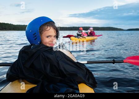 Adolescente caucasica ragazza in casco protettivo stanco ma felice in kayak viaggio siede in un kayak sul lago in estate sera dopo giornata pesante in Carelia, Foto Stock