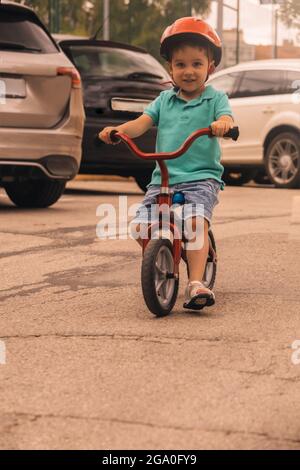 preschooler sorridente e imparare a guidare una bicicletta con il casco mentre si guida intorno alle auto concetto di sicurezza stradale pericolo Foto Stock