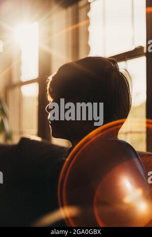 Silhouette di ragazzo in interni con un grande sole flare in angolo. Foto Stock