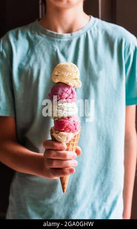 Primo piano della mano del bambino che tiene il cono grande del gelato multi-cucchiaio. Foto Stock
