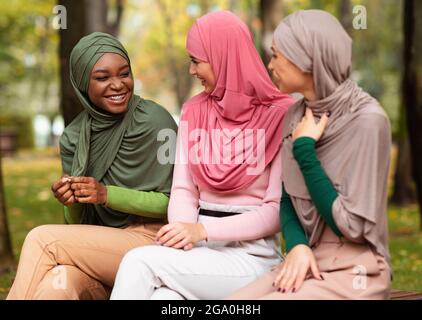 Donne islamiche multietniche che parlano seduto sul banco nel parco all'aperto Foto Stock