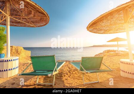 Ombrelloni e due sdraio vuote sulla spiaggia di sabbia con vista sul mare blu, Egitto. Foto Stock