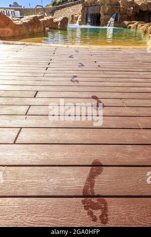 Le orme di closeup sul pavimento di legno dietro la piscina con cascata artificiale su un bellissimo resort in Egitto Foto Stock