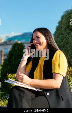 Giovane donna di affari che scrive e parla al telefono sulla strada Foto Stock