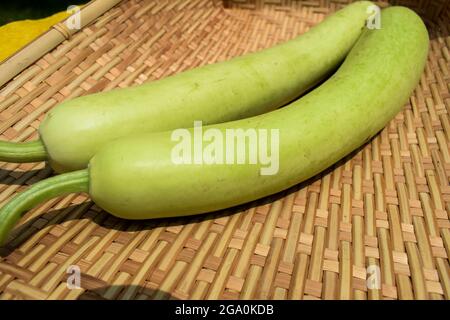 Bottlegourds o bianco-fiore gourd anche conosciuto come calabash sono lunghi e sottili meloni. indiano asiatico verdure in bambù vimini cesto di sfondo Foto Stock