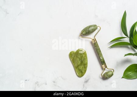 Jade Roller e massaggiatore di pietra gua sha per il viso. Foto Stock