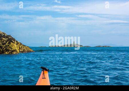 Kayak di mare al largo della costa di Anglesey con Rhoscolyn Beacon in Distance , Galles del Nord, Regno Unito Foto Stock