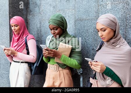 Diverse Signore islamiche che usano telefoni che si levano in piedi sopra la parete grigia all'aperto Foto Stock