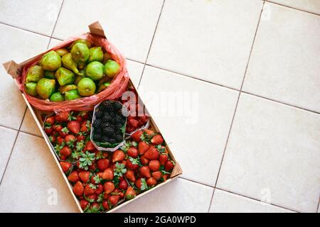 Su una mattonella leggera si trova una cassa con scatole di fragole, lamponi, fichi e more Foto Stock