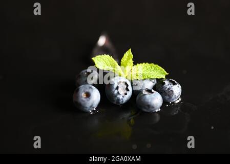 berry mirtillo selvatico su sfondo nero con gocce e menta foglia Foto Stock