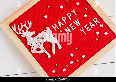 Cartellone con lettera in feltro rosso con testo Felice anno nuovo cervo bianco e sprincle di zucchero su sfondo bianco. Biglietto d'auguri natalizio per le vacanze invernali. Foto Stock